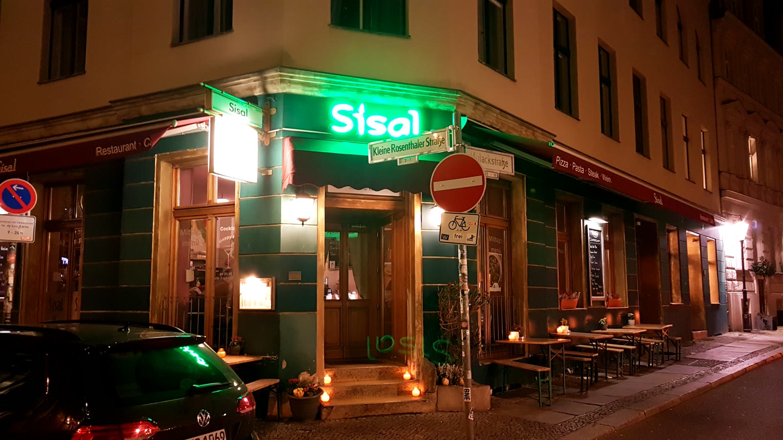 Das Sisal bei Nacht: grüner Neon-Schriftzug über dem Eingang, Kerzen auf den Stufen und Tischen draußen