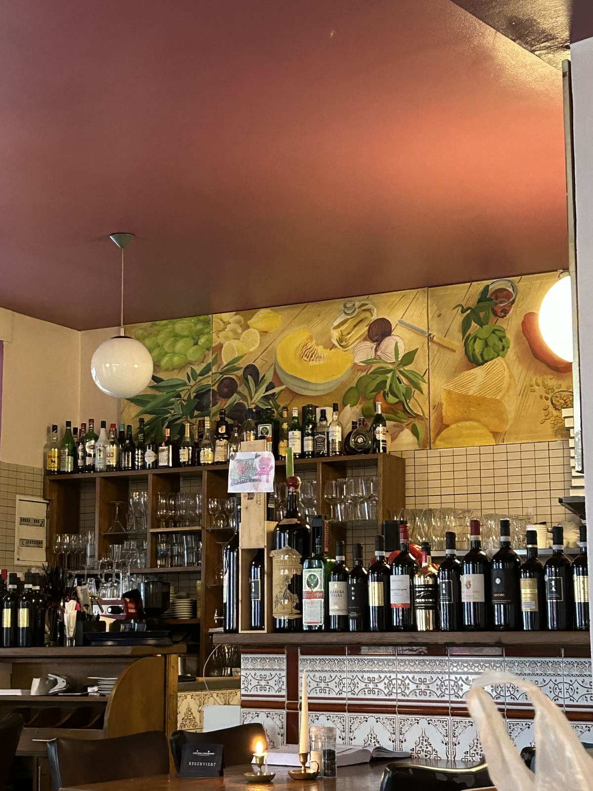 Die Bar im Sisal mit Weinflaschen, Wandmalerei und einer brennenden Kerze auf dem Tisch
