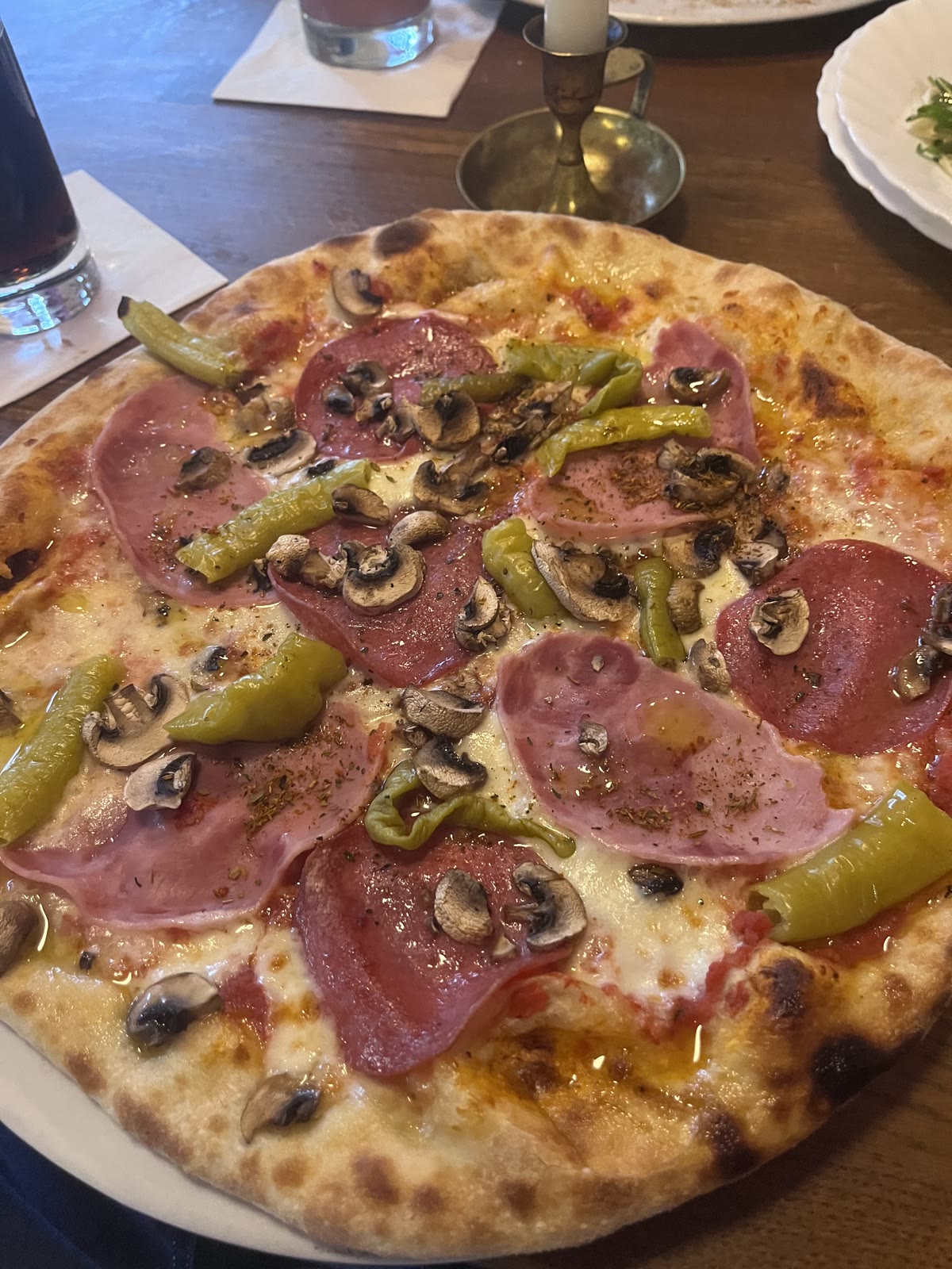 Pizza mit Salami, Schinken, Champignons und Peperoni, daneben ein Kerzenständer