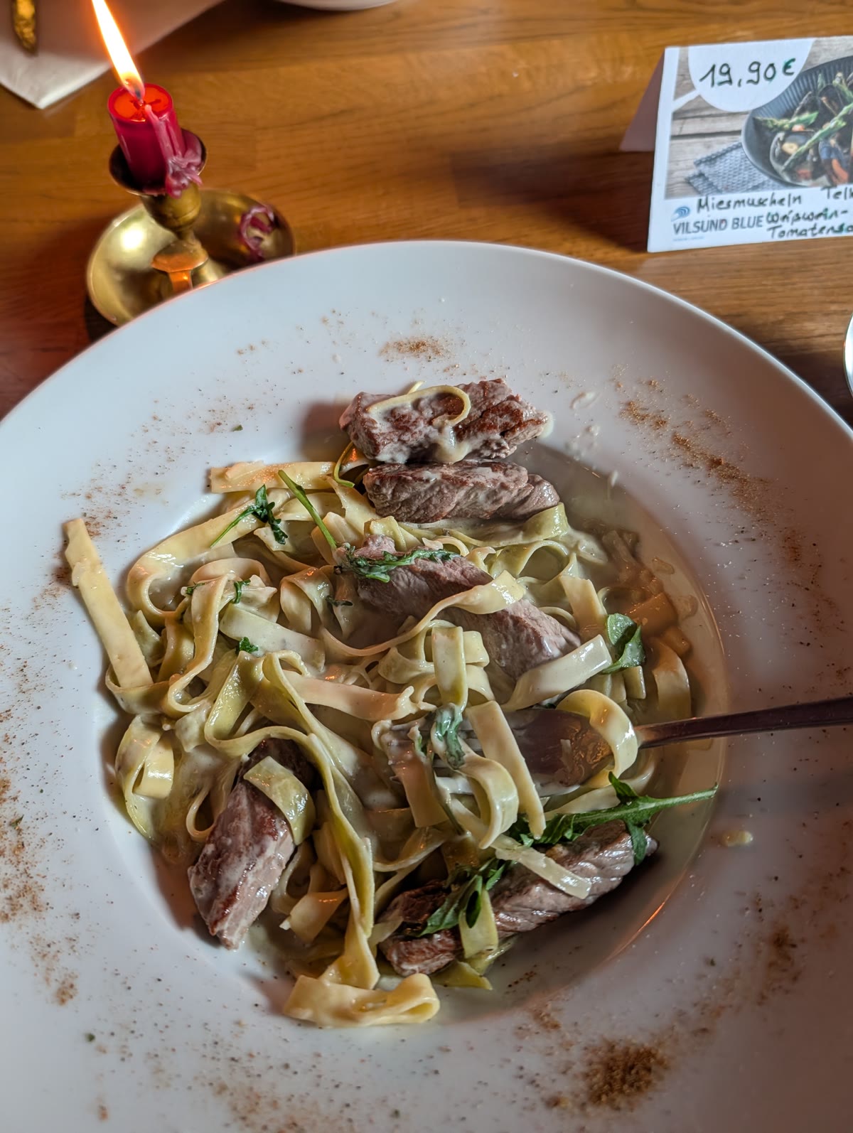 Tagliatelle mit Rindfleischstreifen und Rucola, daneben eine brennende Kerze