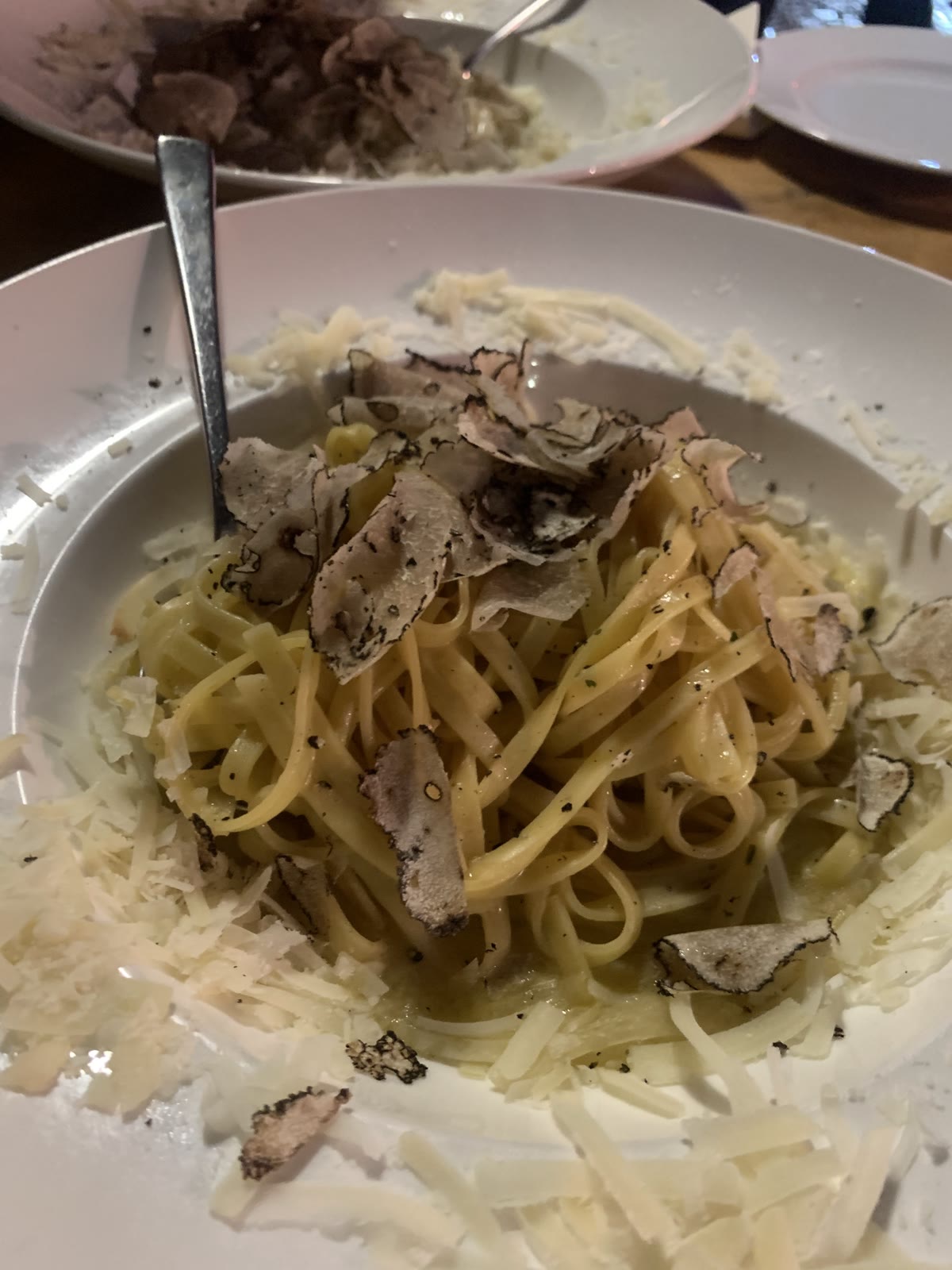 Tagliolino mit frisch gehobeltem Trüffel und Parmesan auf einem weißen Teller